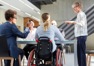 Group of people working around a desk, with one person in a wheelchair