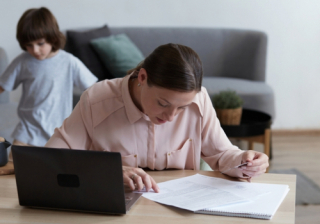 Person filling in finances on a notepad with a child playing behind them