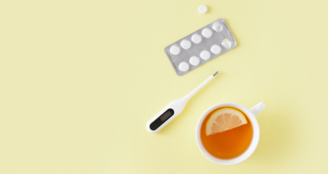 thermometer, medication and a cup of tea on a yellow background